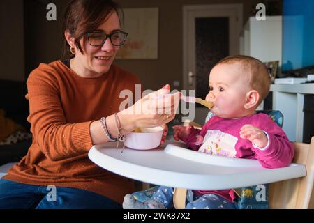 La mamma dà da mangiare alla bambina di 6 mesi con una purea di alimenti per bambini. Foto Stock