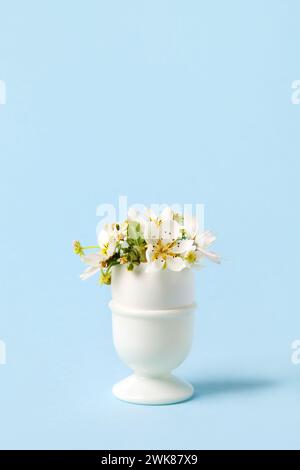 Uovo bianco in un piedistallo con pera primaverile e fiori di fragola su sfondo blu. Buona Pasqua Foto Stock