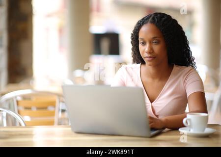 Donna nera che scrive su un computer portatile in una terrazza di una caffetteria Foto Stock