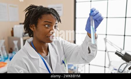 Scienziata africana che analizza una provetta in un ambiente luminoso di laboratorio. Foto Stock