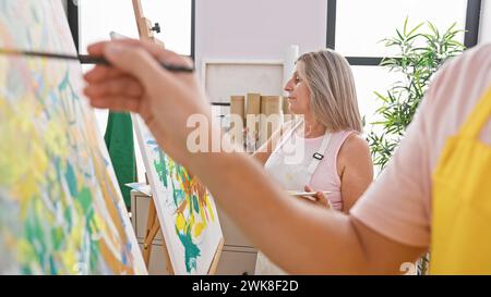 Due artisti, un uomo e una donna, che approfondiscono profondamente la loro arte! riuniti in uno studio accogliente, la creatività senza ostacoli si sviluppa su tela. Foto Stock