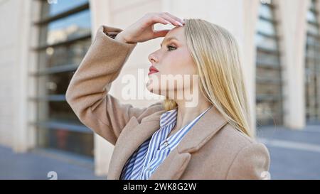 Una donna bionda in abiti da lavoro guarda con cura all'aperto in un ambiente cittadino. Foto Stock