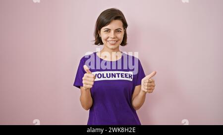 Giovane donna ispanica entusiasta, volontaria lampeggia con un gesto sicuro del pollice, sfoggia capelli corti e uniforme di beneficenza, isolando orecchio-orecchio Foto Stock