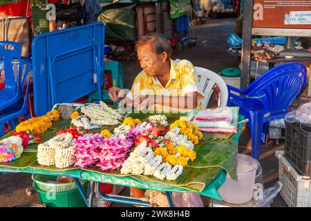 Bangkok, Tailandia - 4 gennaio 2010: Una vecchia donna intreccia i fiori alla corona di fiori che vengono utilizzati nel tempio e come decorazione religiosa. Foto Stock