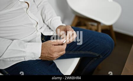 Uomo maturo che piega il biglietto in una luminosa sala d'attesa, raffigurando pazienza e attesa in un ambiente interno. Foto Stock