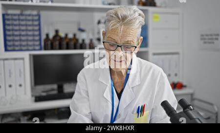 Donna anziana scienziata dai capelli grigi che indossa gli occhiali, coinvolta in un cruciale lavoro di laboratorio di ricerca medica Foto Stock