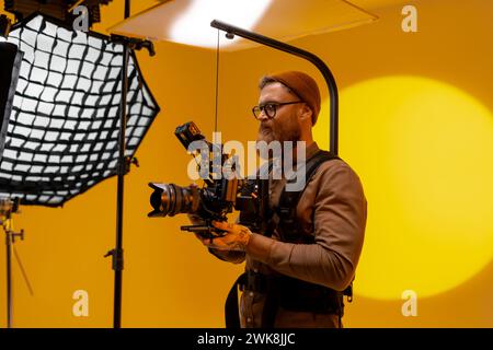 Uomo che tiene una fotocamera davanti a sfondo giallo Foto Stock