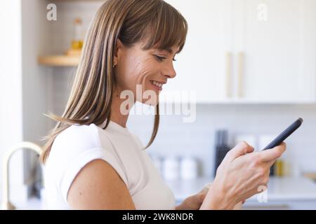 Una donna caucasica di mezza età sorride mentre guarda il suo smartphone Foto Stock