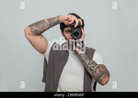 Handsome Man Professional con tatuaggio con cappello in maglia con maglione in maglia che regge la fotocamera senza specchio e scatta foto in Studio Foto Stock