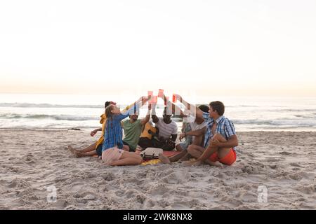 Diversi gruppi di amici brindano su una spiaggia al tramonto, facendo una festa Foto Stock
