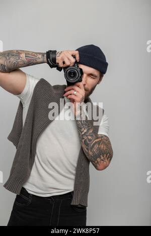 Fotografo professionista elegante e alla moda con tatuaggio, cappello e maglione in maglia, con fotocamera Mirrorless e foto i Foto Stock