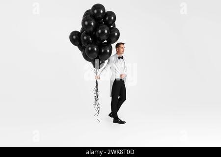 elegante uomo d'affari caucasico in smoking bianco con balloni all'elio su sfondo bianco. Foto Stock