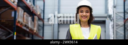 supervisore di magazzino felice con elmetto e giubbotto di sicurezza focalizzato sul tablet digitale durante il lavoro, banner Foto Stock