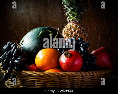 La frutta assortita in un cestino su un vecchio tavolo di legno sullo sfondo marrone noce. Foto Stock