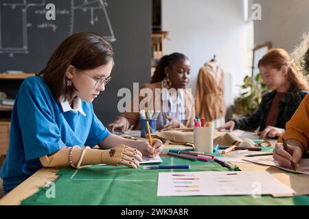 Vista laterale ritratto di una ragazza adolescente con protesi che disegnano a mano schizzi di abiti in classe sartoriale Foto Stock