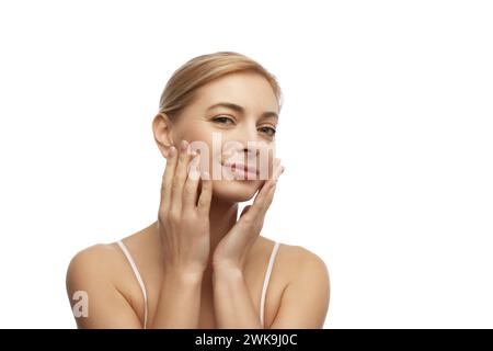 Bella, giovane donna tocca la sua pelle facciale e si gode la sua pelle idratata e morbida dopo le procedure spa su sfondo bianco studio. Foto Stock