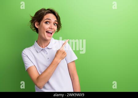 Foto attraente giovane donna stupita consiglia di iscriversi al canale dei social media in cui pubblica codici promozionali isolati su sfondo di colore verde Foto Stock