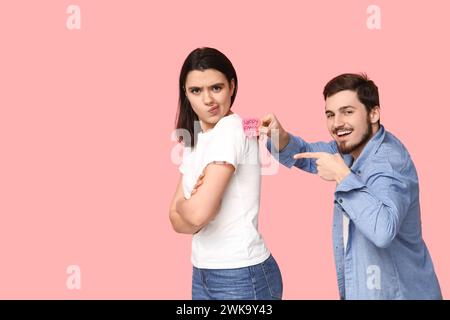 Giovane che attacca carta sulla schiena del suo amico su sfondo rosa. Festa del giorno dello scemo d'aprile Foto Stock