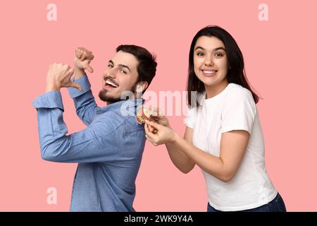 Giovane donna che attacca il pesce di carta sulla schiena della sua amica su sfondo rosa. Festa del giorno dello scemo d'aprile Foto Stock