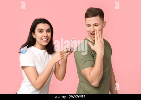 Giovane donna che attacca il clown di carta sulla schiena della sua amica su sfondo rosa. Festa del giorno dello scemo d'aprile Foto Stock