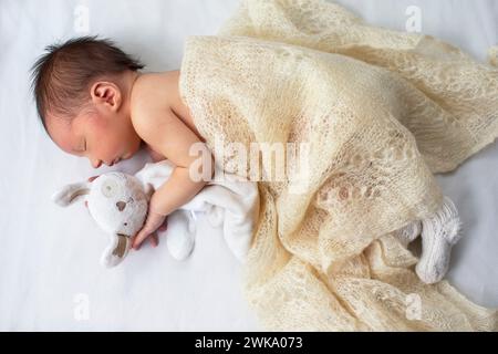 Neonato con un morbido coniglietto giocattolo su sfondo bianco. Foto Stock