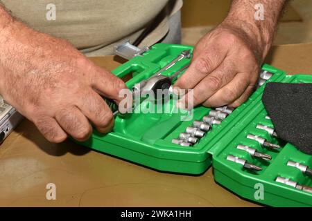 Primo piano delle mani di un lavoratore che prepara una chiave a cricchetto per fabbro per il lavoro, collega la chiave alla testa a bussola. Foto Stock