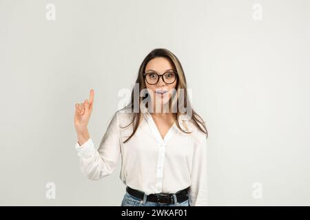 Una giovane donna sorpresa con lunghi capelli marroni e grandi occhiali, che indossa una camicetta bianca e un paio di jeans Foto Stock