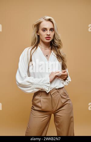 giovane donna bionda in abiti casual dallo stile classico che guarda la fotocamera in beige, alla moda senza tempo Foto Stock