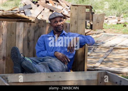 falegname afroamericano sul suo posto di lavoro , appoggiato su una panchina di legno, sta facendo case wendy sul lato della strada Foto Stock