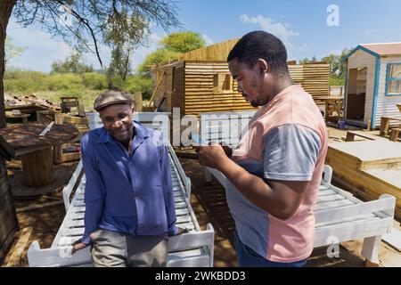 falegname afroamericano che negozia con il cliente di fronte a una casa wendy, capanna di legno all'aperto, primo piano, si trova sul letto fatto di w Foto Stock