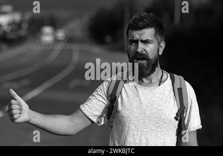 Corsa arresto automatico. Concetto di avventura e turismo. Uomo in abbigliamento casual ondeggiante auto, hitchhiking su strada. Viaggiando in auto-stop, avendo viaggio estivo Foto Stock