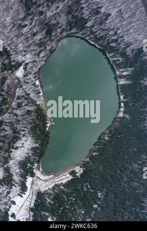 Vista aerea con droni di un lago vulcanico in inverno. Sorvolando il lago Sfanta Ana, il lago Szent Anna, Szeklerland, Transilvania, Romania Foto Stock