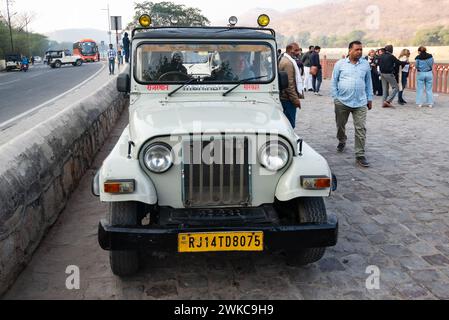 Amer, Jaipur, India. 16 febbraio 2024. Vivace scena di strada con turisti e guide che si riuniscono intorno a una jeep bianca che li trasporterà al famoso Foto Stock