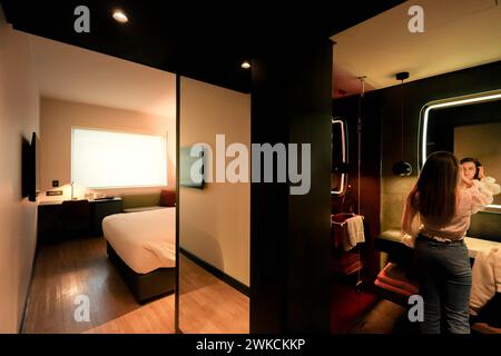 Un ospite si erge in una camera d'hotel contemporanea con decor minimalista, catturata in un momento di comfort ed eleganza. Foto Stock