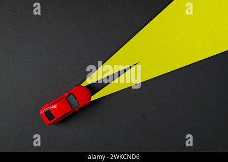 Vista dall'alto dell'auto giocattolo rossa e dei fari gialli su sfondo grigio scuro Foto Stock