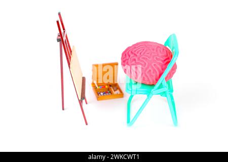 Modello di cervello umano seduto su una sedia pieghevole di tè accanto a un cavalletto, accompagnato da una scatola di colori vivaci. Intelligenza artificiale e arte digitale conc Foto Stock