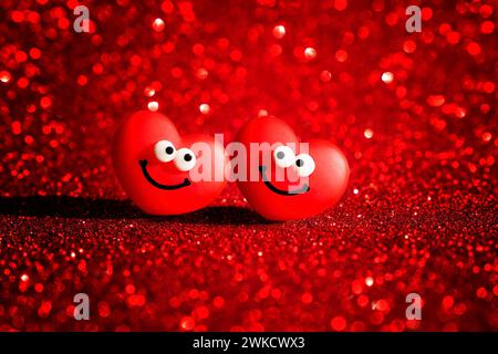 Due personaggi di cuore sorridenti irradiano gioia su uno sfondo rosso scintillante, creando il biglietto di San Valentino perfetto. Foto Stock