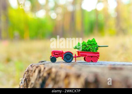 Il trattore giocattolo trasporta un piccolo albero verde arroccato in cima a un vecchio ceppo di alberi nel cuore della foresta. Concetto relativo alla registrazione industriale. Foto Stock