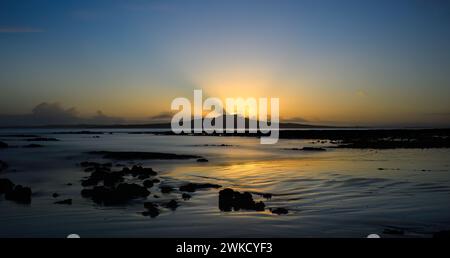I raggi di sole brillano sulla cresta dell'isola di Rangitoto mentre il sole sorge. Milford Beach. Auckland. Foto Stock