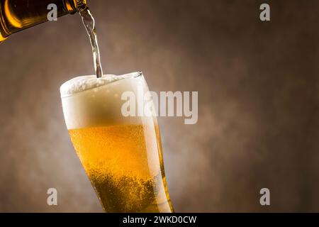 Versare birra lager nel bicchiere con schiuma su sfondo scuro. Foto Stock