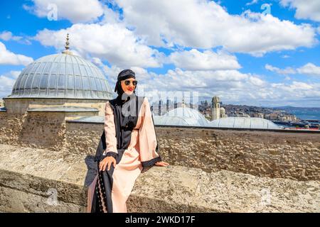 Seduta su un muro di pietra alla Moschea Suleymaniye, una donna con un costume arabo hijab gode di una vista panoramica di Istanbul. Tranquillità e armonia del Foto Stock