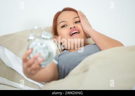 una donna che si sveglia tardi la mattina e spegne la sveglia Foto Stock