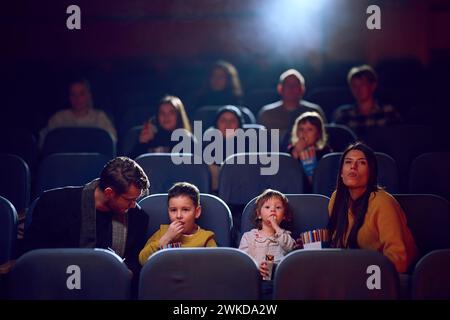 Una famiglia moderna ama trascorrere momenti di qualità insieme al cinema, viziandosi con popcorn mentre guarda un film con i propri figli Foto Stock