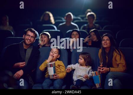 Una famiglia moderna ama trascorrere momenti di qualità insieme al cinema, viziandosi con popcorn mentre guarda un film con i propri figli Foto Stock