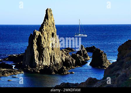 Una vista serena che cattura una barca a vela che passa davanti a maestose formazioni rocciose lungo la costa, adagiata contro un oceano blu vibrante Foto Stock