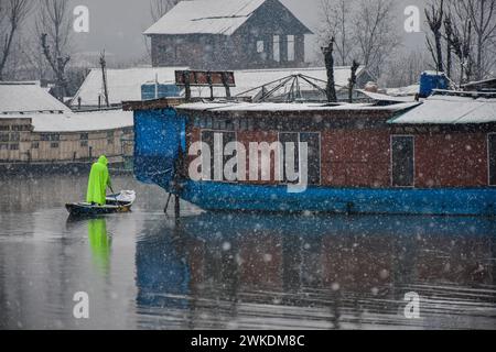 Srinagar, India. 20 febbraio 2024. Un barcaiolo che indossa un impermeabile affonda la sua barca attraverso il lago dal durante le forti nevicate a Srinagar.la città di Srinagar ha ricevuto nevicate martedì, mentre i tratti più alti del Kashmir hanno assistito a abbondanti nevicate nelle ultime 48 ore, come hanno detto i funzionari qui. La National Highway rimase chiusa e i servizi di volo da e per Srinagar furono cancellati. Credito: SOPA Images Limited/Alamy Live News Foto Stock