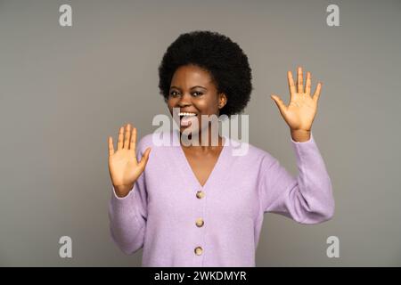 Donna nera positiva sorridente divertiti, mostrando palme che urtano contro un muro invisibile come un mimo in studio Foto Stock