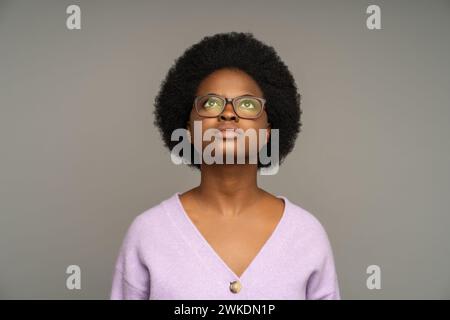 Donna afroamericana premurosa e premurosa, attenta a guardare verso l'alto, isolata sullo sfondo dello studio Foto Stock