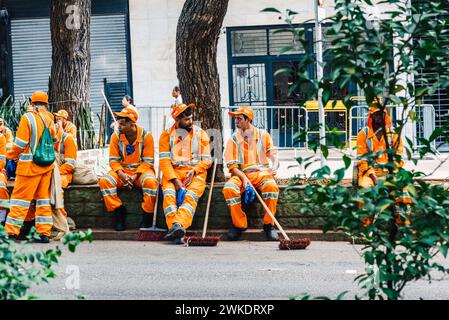 Un certo numero di operatori sanitari rivestiti in distintive uniformi arancioni sono seduti e riposati su un marciapiede a San Paolo, in Brasile Foto Stock