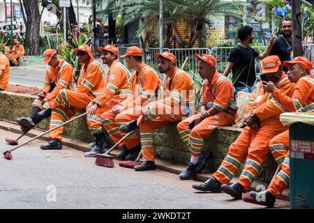 Un certo numero di operatori sanitari rivestiti in distintive uniformi arancioni sono seduti e riposati su un marciapiede a San Paolo, in Brasile Foto Stock